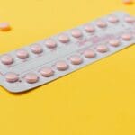 A blister pack of pink pills placed on a vibrant yellow background, symbolizing medicine and healthcare.