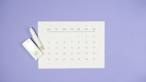 Minimalist setup of a glucometer, lancet pen, and calendar on a light purple background.